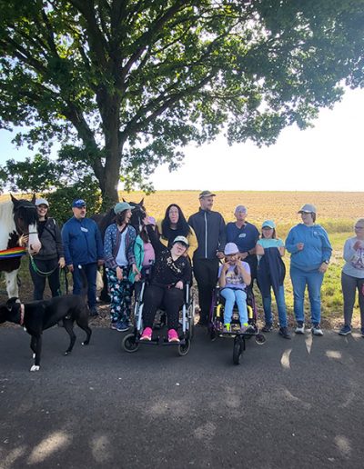 Eine Gruppe von etwa zwölf Personen, darunter einige in Rollstühlen, steht unter einem Baum